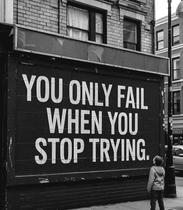 Black and white street mural with the text ‘You only fail when you stop trying’ and a child looking up at it.